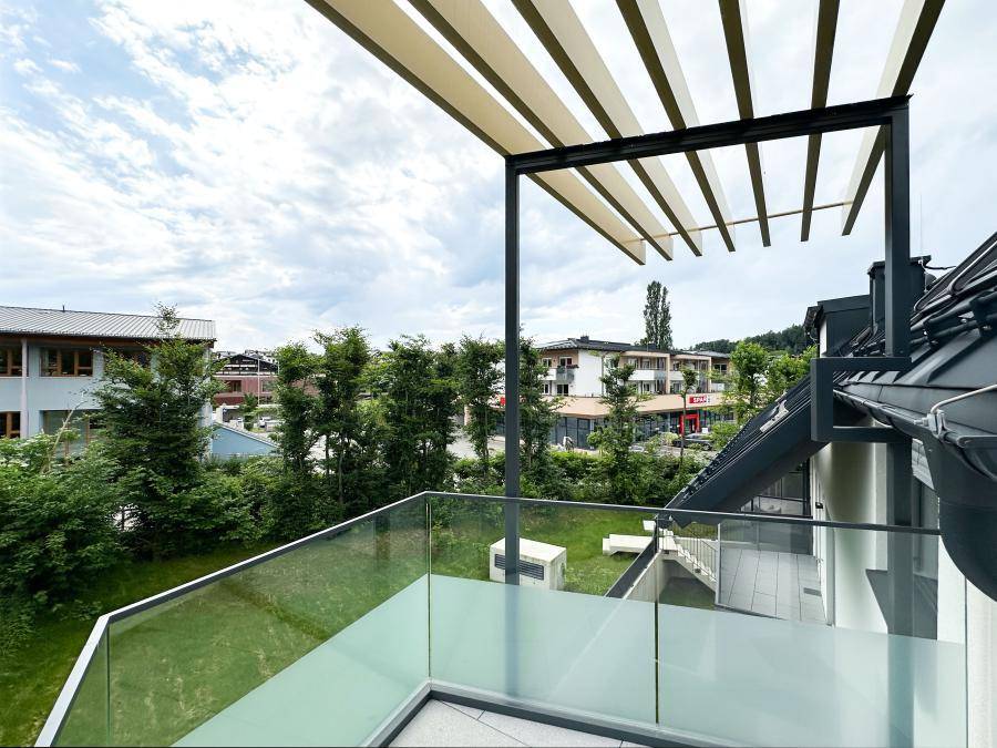 Moderner Balkon mit Glasgeländer und Blick auf die umliegende Bebauung und grüne Umgebung.