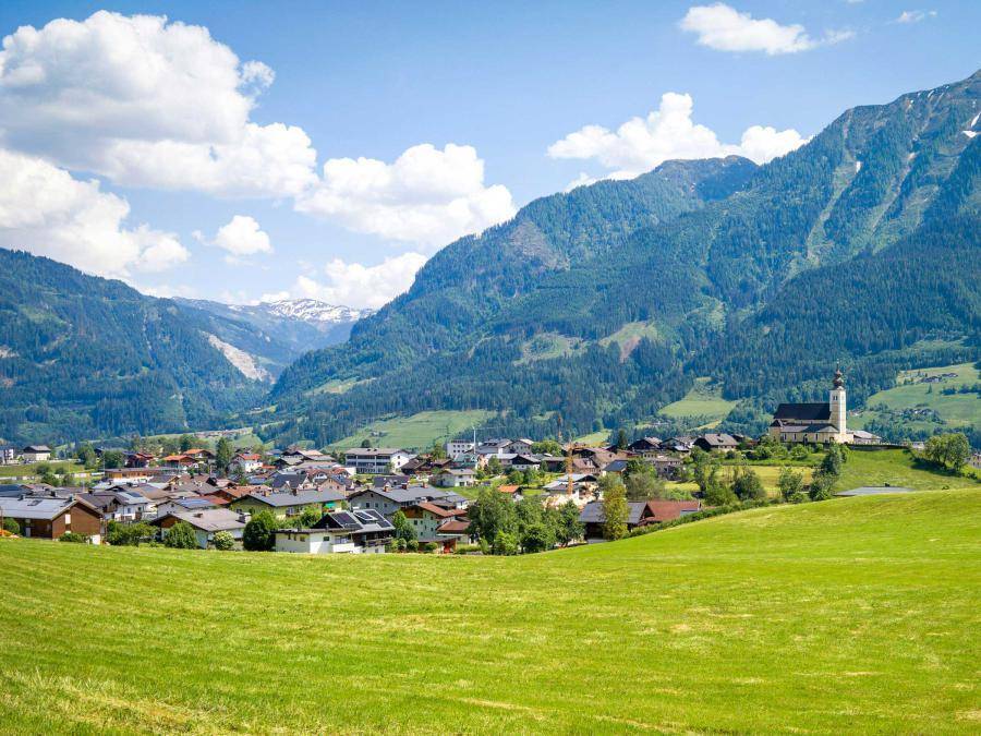 Panoramablick auf ein malerisches Dorf in einem grünen Tal, umgeben von majestätischen Bergen.