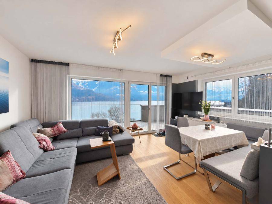 Gemütlicher Wohn- und Essbereich mit großem Sofa, Holzboden und beeindruckendem Blick auf den See und die Berge.