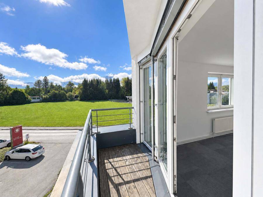 Geräumiger Balkon mit Holzboden und Metallgeländer, bietet einen weiten Blick ins Grüne.