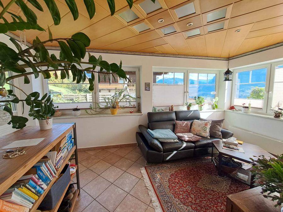 Gemütliches Wohnzimmer mit Fliesenboden, Ledersofa und Holzdecke, hell durch große Fenster.