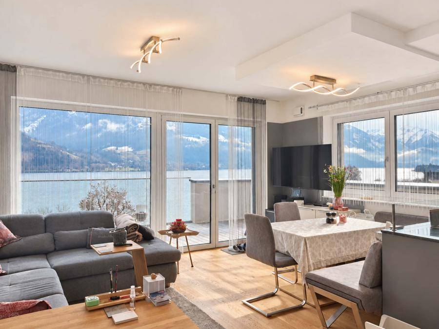 Heller Wohn-Essbereich mit großen Fenstern, die einen weiten Blick auf den See und die umliegende Berglandschaft bieten.