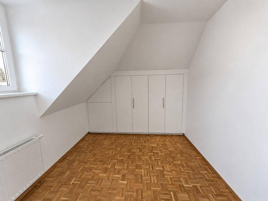 Geräumiges Dachzimmer mit Parkettboden und maßgefertigten Einbauschränken, die den Raum optimal nutzen.