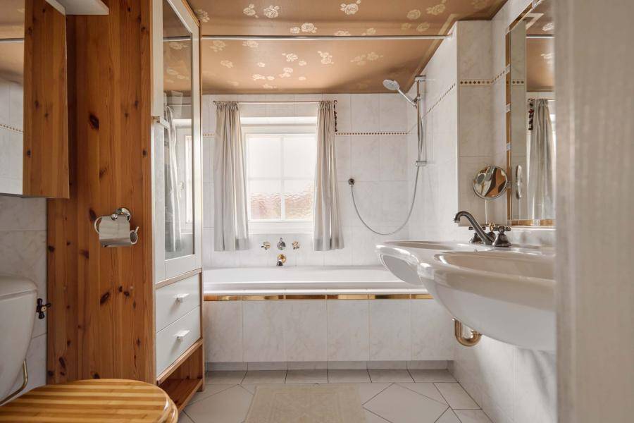 Traditionelles Badezimmer mit Badewanne, Doppelwaschbecken und Fenster, hell gefliest.