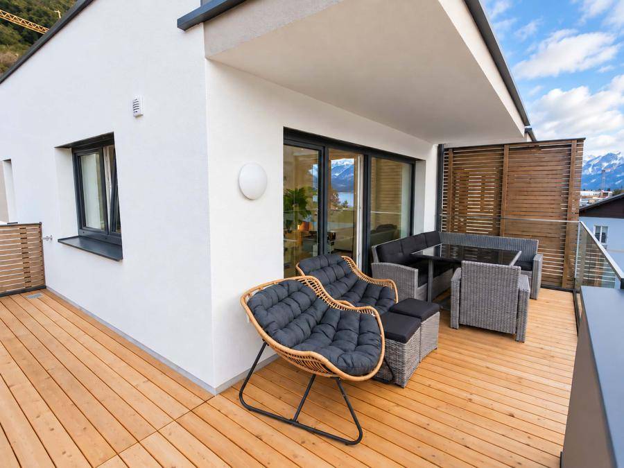 Möblierter Balkon mit Holzboden und bequemen Sitzgelegenheiten, ideal für entspannte Stunden mit Seeblick.