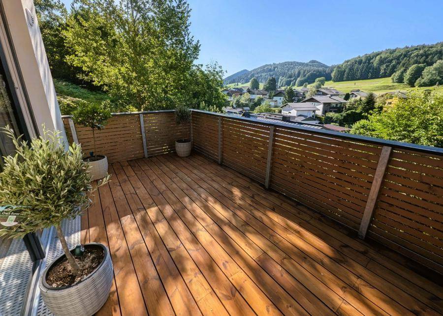 Geräumiger Holzbalkon mit Topfpflanzen und sonnigem Ausblick auf die bewaldeten Hügel.