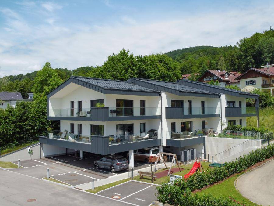 Moderne Wohnanlage mit mehreren Balkonen, Carports und einem Spielplatz, eingebettet in grüne Hügel.