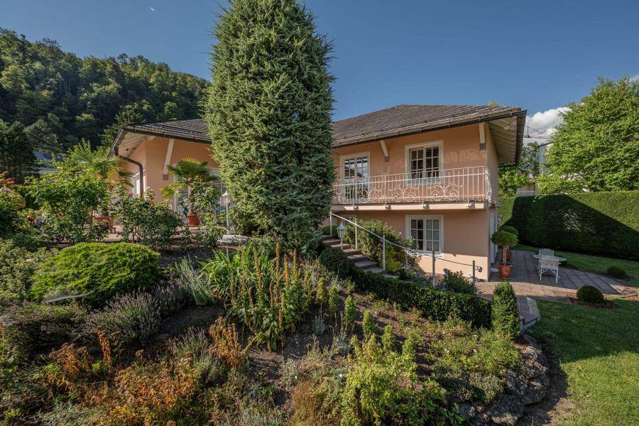 Attraktives Haus mit terrassiertem Garten und üppiger Bepflanzung unter blauem Himmel.