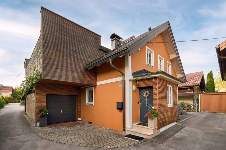 Vorderansicht des Hauses mit integrierter Garage, Holzverkleidung und gepflastertem Zugang.