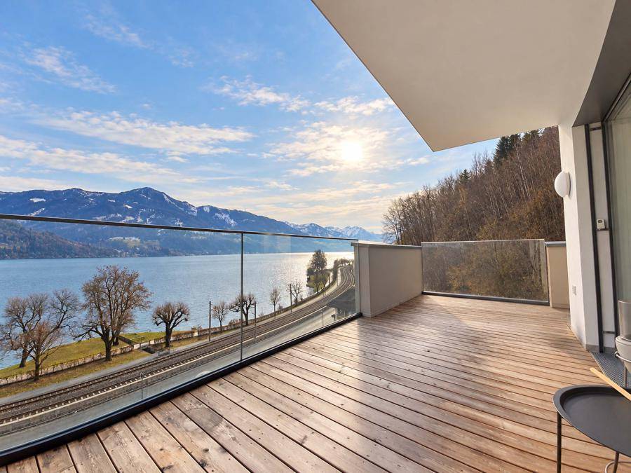 Geräumige Holzterrasse mit modernem Glasgeländer und weitem Blick über den See und die umliegende Landschaft.