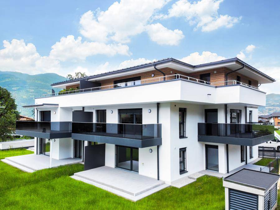 Ansicht der modernen Wohnanlage mit weißen Fassaden, großen Balkonen und Bergblick im Hintergrund.