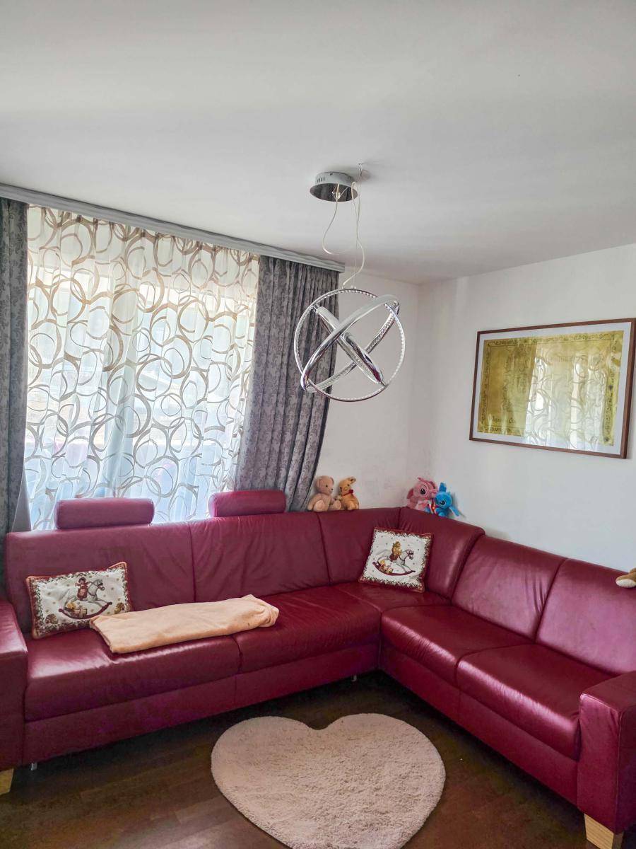 Gemütliches Wohnzimmer mit rotem Ledersofa, dunklem Holzboden und dekorativer Beleuchtung.