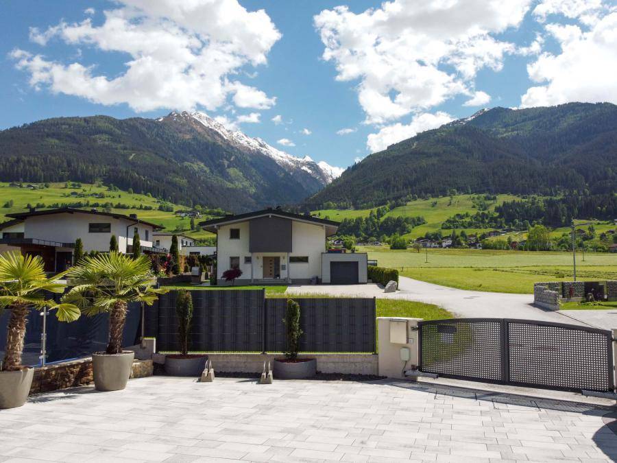 Einfahrt eines modernen Hauses mit Blick auf die umliegende Berglandschaft unter blauem Himmel.