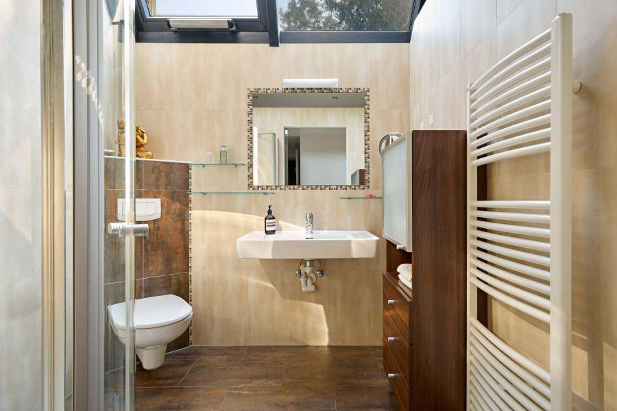 Modernes Badezimmer mit begehbarer Dusche, Wand-WC, Dachfenster und beigen Fliesen.