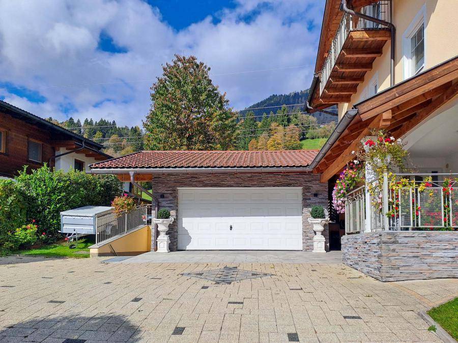 Doppelgarage mit Zufahrt und gepflastertem Vorplatz, umgeben von grüner Bepflanzung.