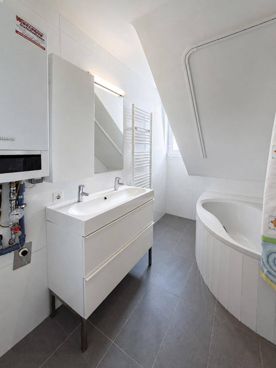 Modernes Badezimmer mit Doppelwaschbecken, Badewanne unter der Dachschräge und Handtuchheizkörper.