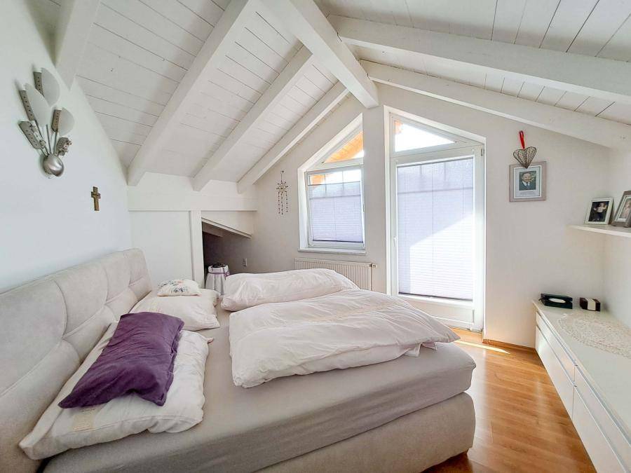 Helles Schlafzimmer im Dachgeschoss mit Holzbalken, schrägen Wänden und großen Fenstern.