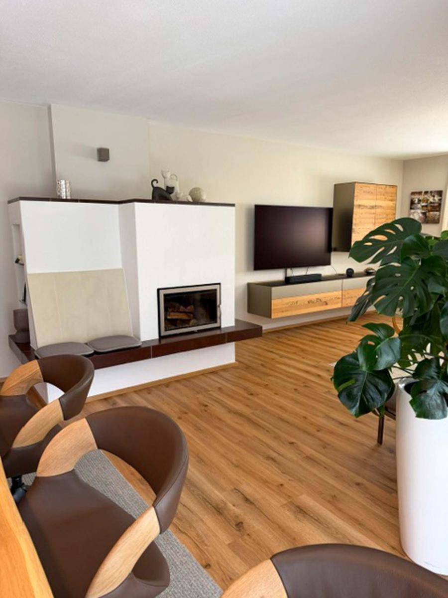 Geräumiges Wohnzimmer mit modernem Kamin, Holzboden und großem Fernseher.