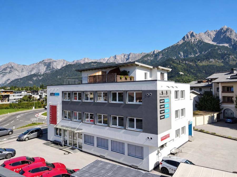 Modernes Geschäftsgebäude mit einer Dachterrasse und beeindruckendem Bergpanorama unter strahlend blauem Himmel.