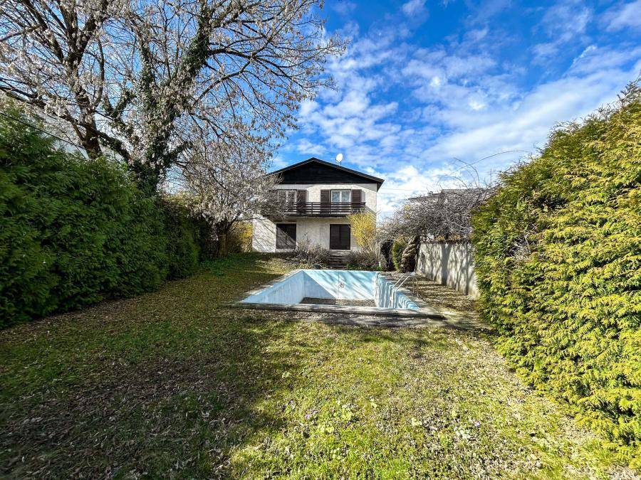 Haus mit großem Garten und leerem Swimmingpool, umgeben von Bäumen und Hecken.