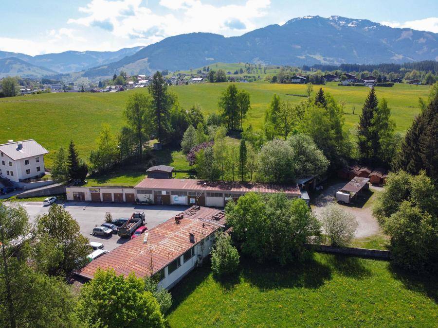 Weitläufige Luftaufnahme des Grundstücks mit Gebäuden, Parkflächen und der malerischen Berglandschaft im Hintergrund.