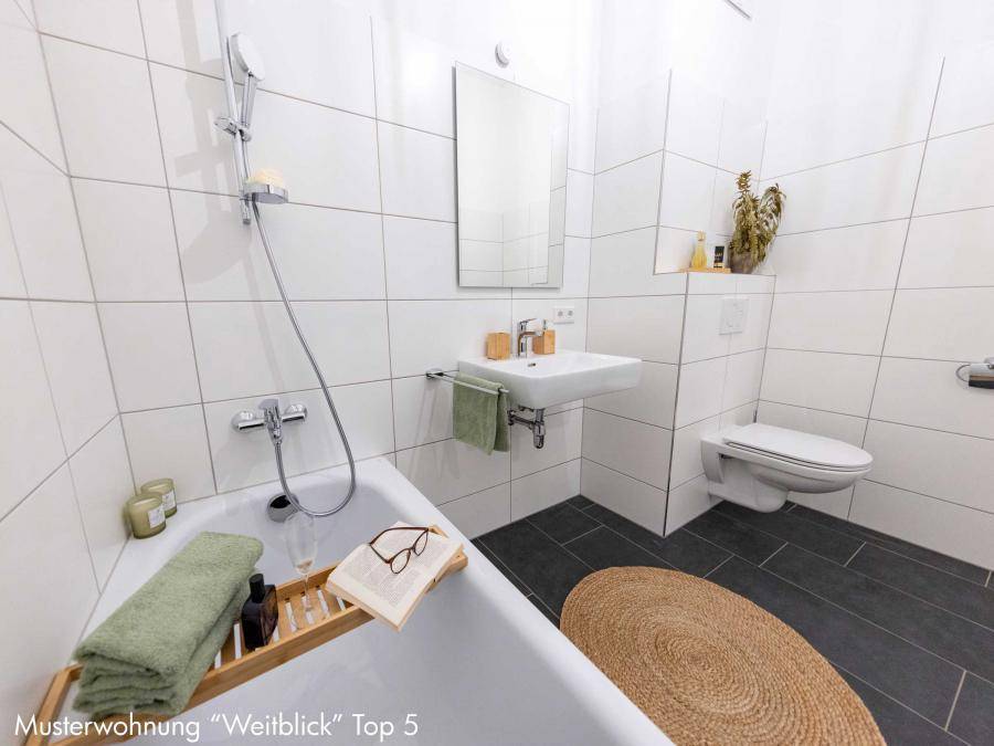 Modernes Badezimmer mit weißen Fliesen, Badewanne und wandhängendem WC.