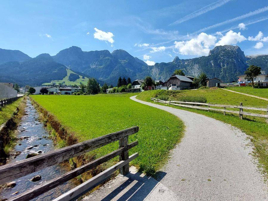 Malerische Landschaft mit einem Feldweg, einem kleinen Bach und majestätischen Bergen im Hintergrund.