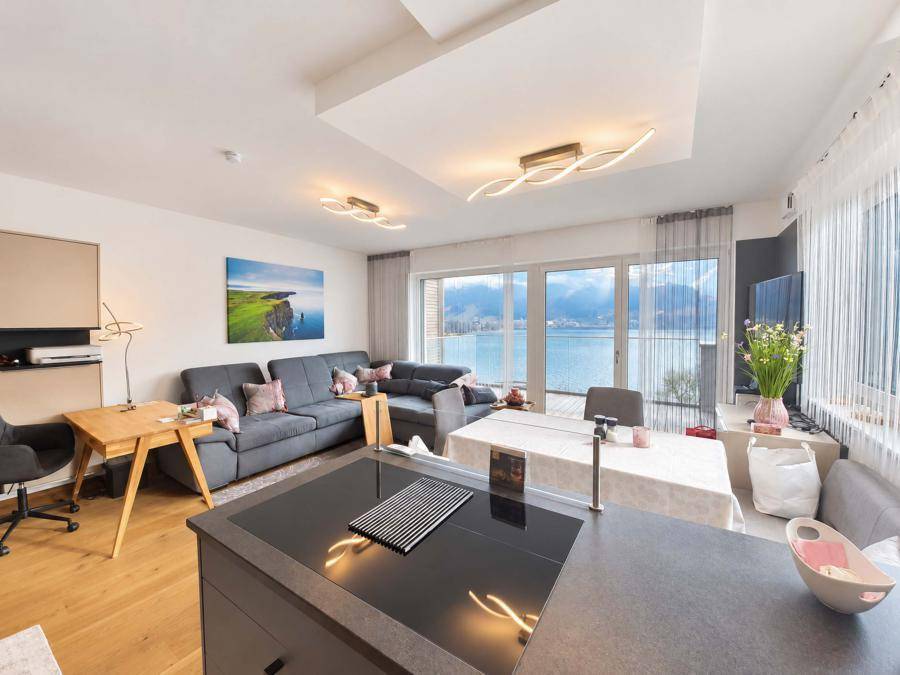 Heller offener Wohn-Essbereich mit moderner Küche, Seeblick und Zugang zum Balkon durch große Fenster.