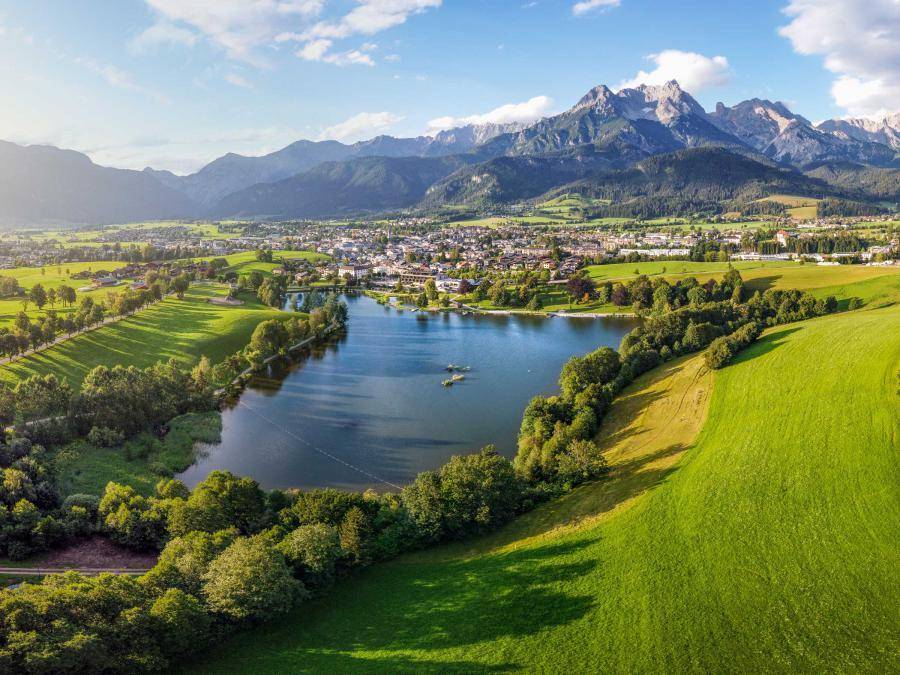 Panoramablick auf eine malerische Stadt am See, umgeben von grünen Hügeln und majestätischen Bergen.