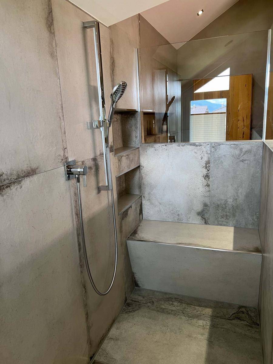 Moderne begehbare Dusche mit Betonoptikwänden und integrierter Sitzbank.