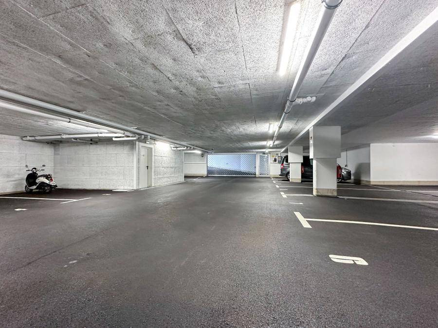 Geräumige und gut beleuchtete Tiefgarage mit markierten Stellplätzen und Motorroller.