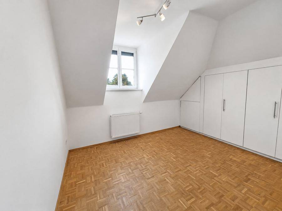 Helles Dachzimmer mit Parkettboden, Fenster und praktischen Einbauschränken entlang der Schräge.