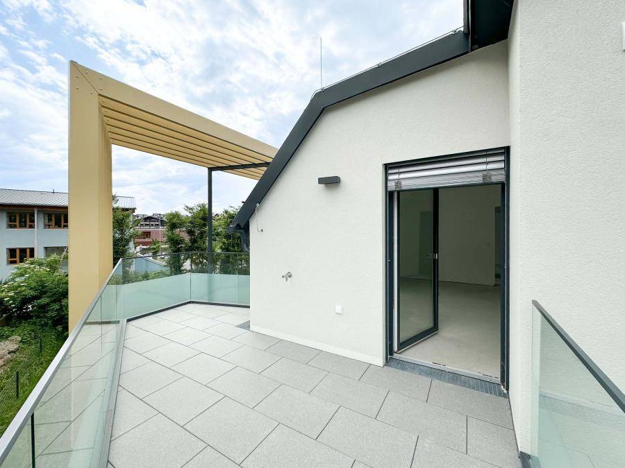 Geräumiger Balkon mit modernem Glasgeländer und Zugang zu einem hellen, unmöblierten Innenraum.