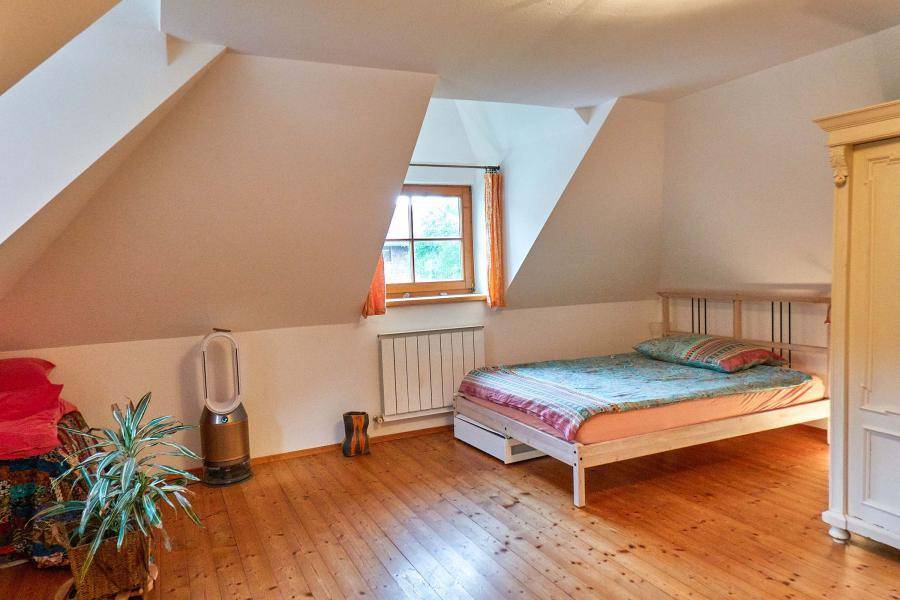 Schlafzimmer mit Holzdielenboden, Dachschräge und einem Fenster mit Blick ins Grüne.