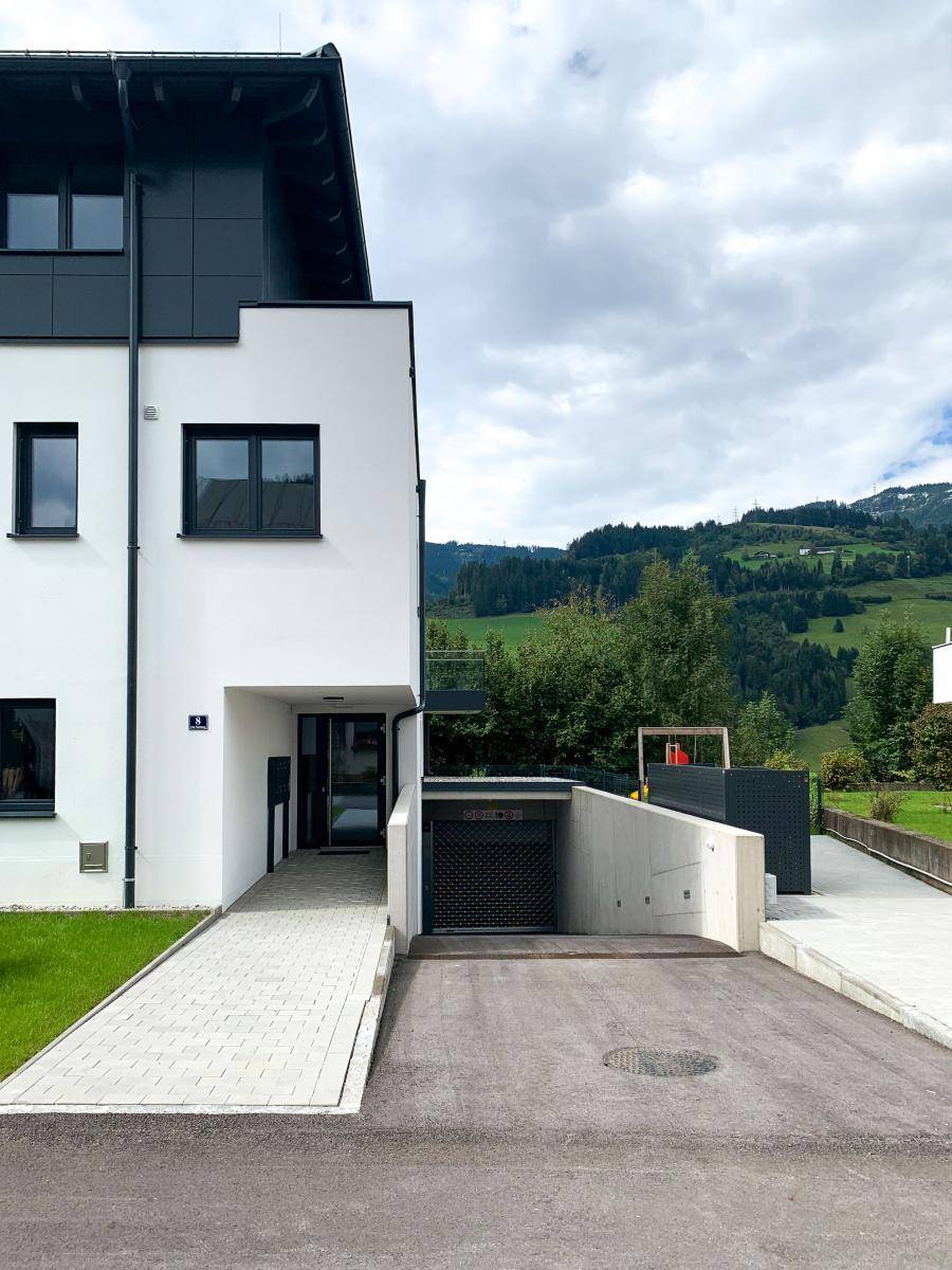 Eingangsbereich eines modernen Neubaus mit Zufahrt zur Tiefgarage und gepflegter Außenanlage.