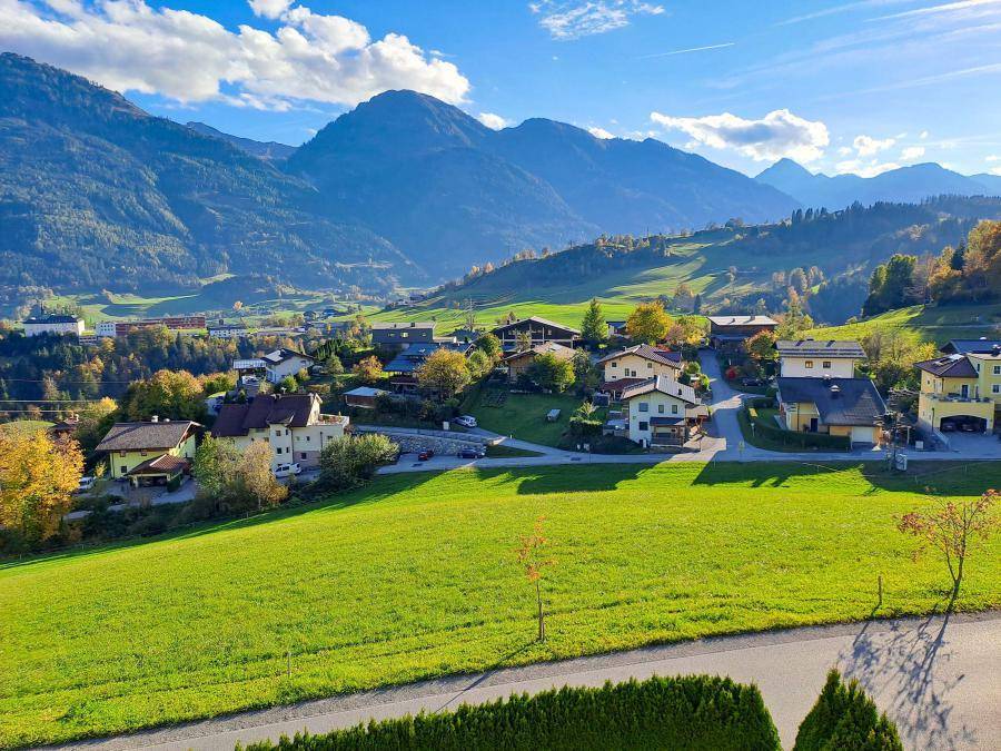 Malerische Landschaft mit weiten grünen Feldern und Häusern vor imposanter Bergkulisse.