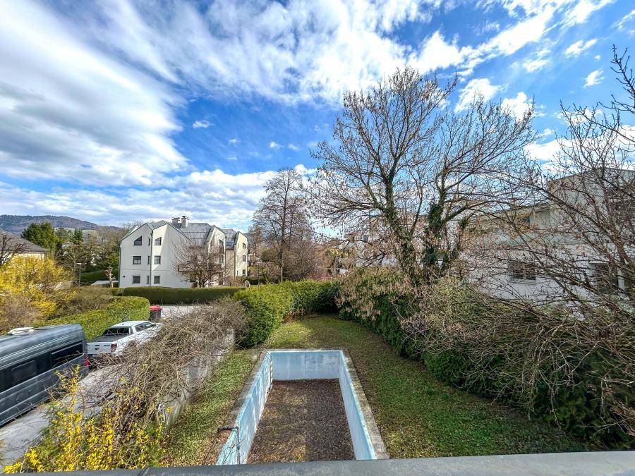 Blick von einem Balkon auf den Garten mit leerem Pool und die umliegende Wohngegend mit Hügeln.
