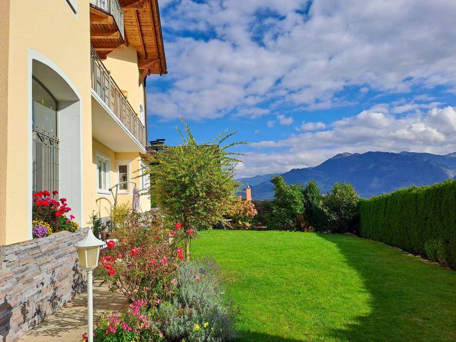Gepflegter Rasenbereich im Garten mit blühenden Sträuchern und weitem Bergblick.