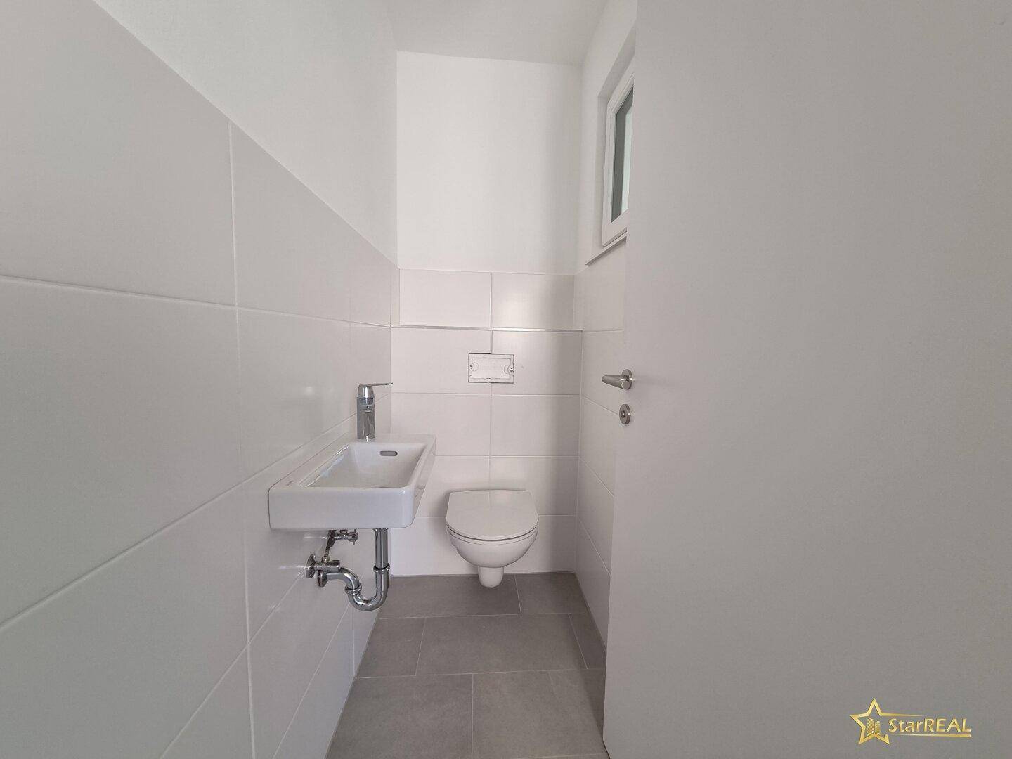 Modernes Gäste-WC mit weißen Fliesen, wandhängendem WC und kleinem Waschbecken.