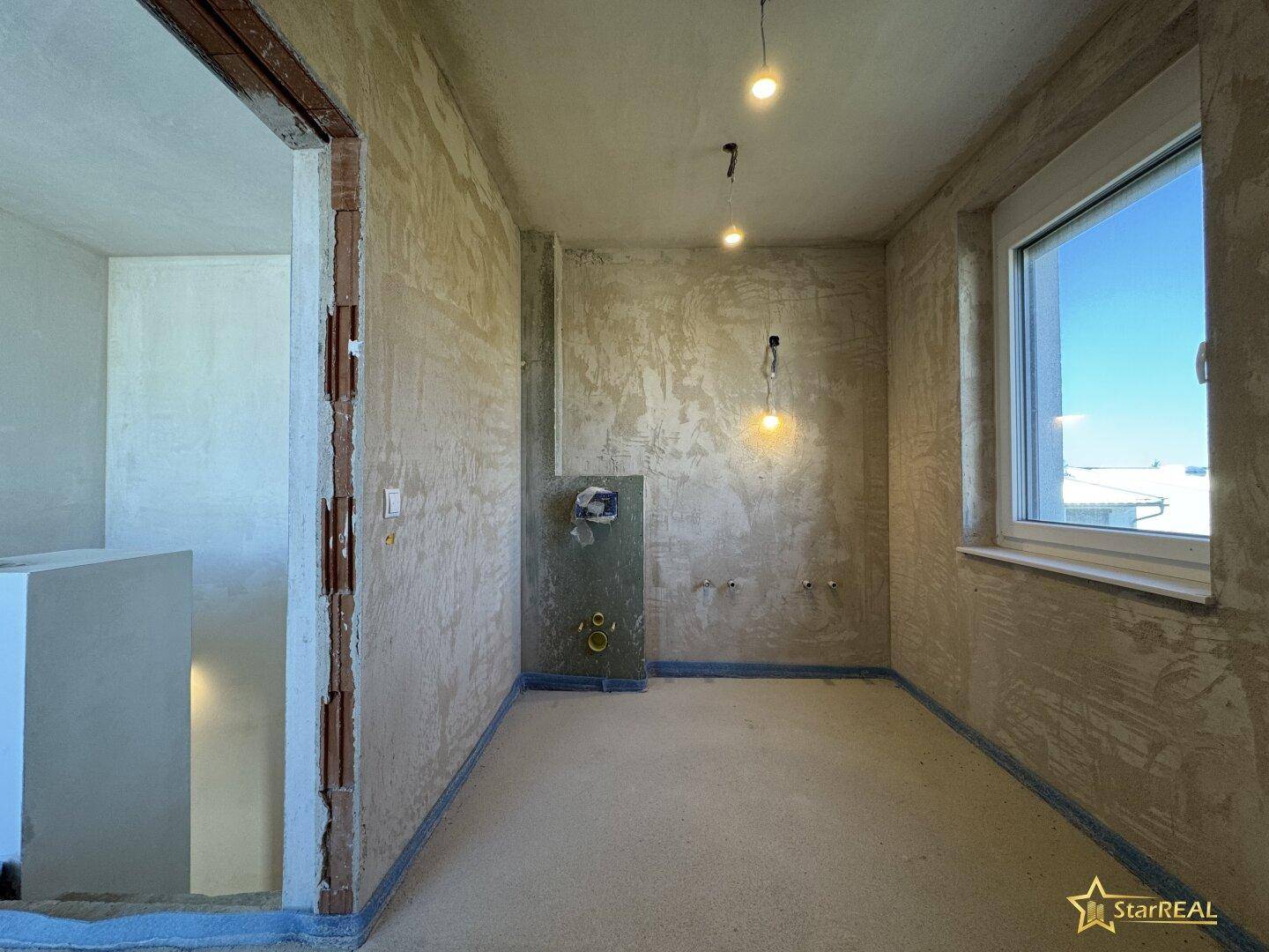 Rohbauzimmer mit Fenster und vorbereiteten Anschlüssen, ideal für ein Badezimmer.