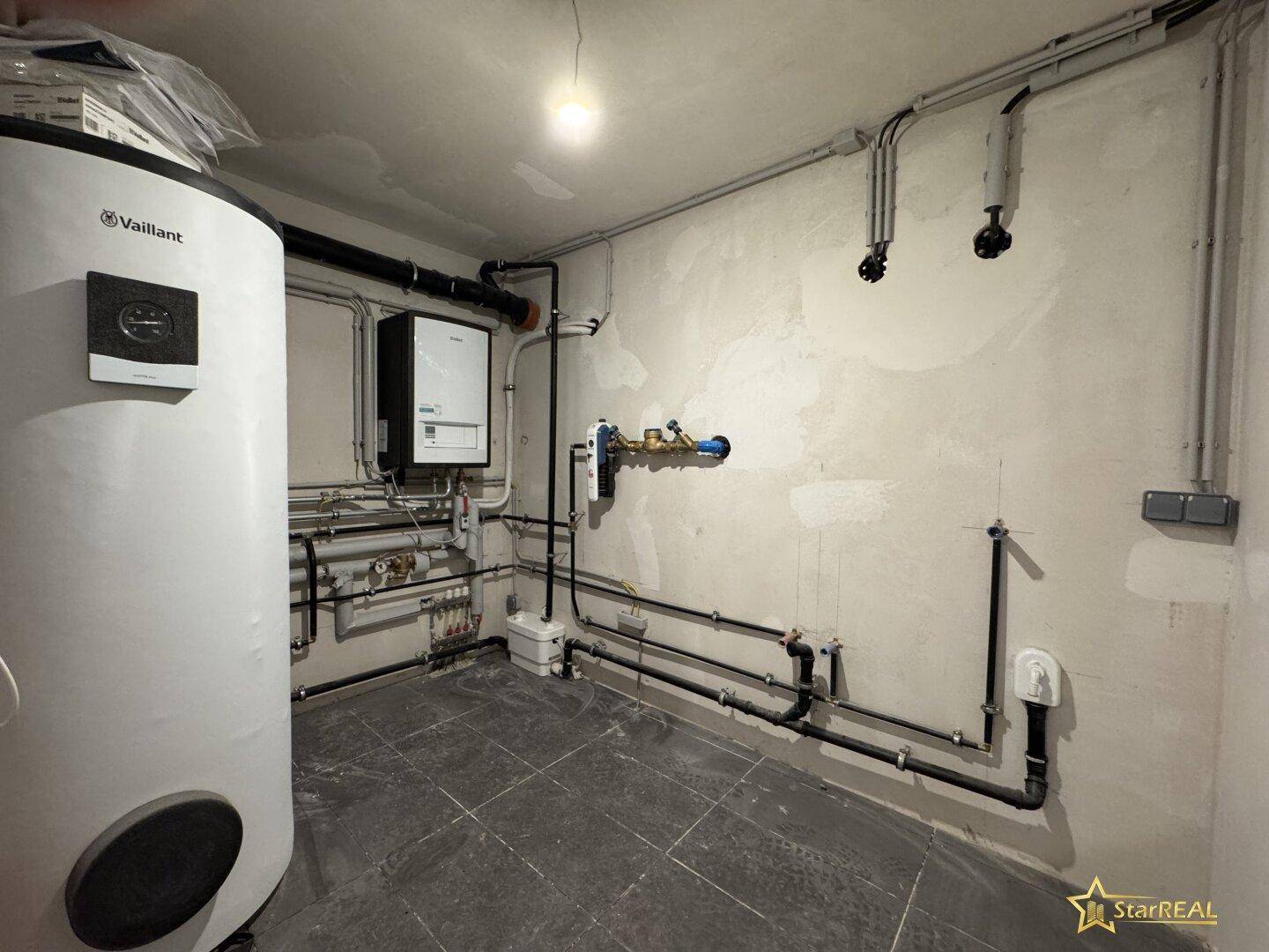 Heizungsraum mit Warmwasserspeicher und sichtbaren Rohrleitungen, funktional und geräumig.