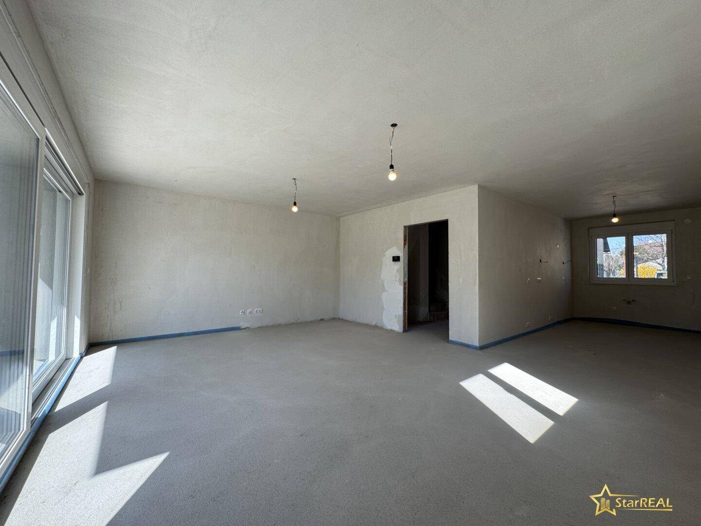 Geräumiger, unfertiger Innenraum mit Betonboden und Rohbauwänden, bereit für den Ausbau.
