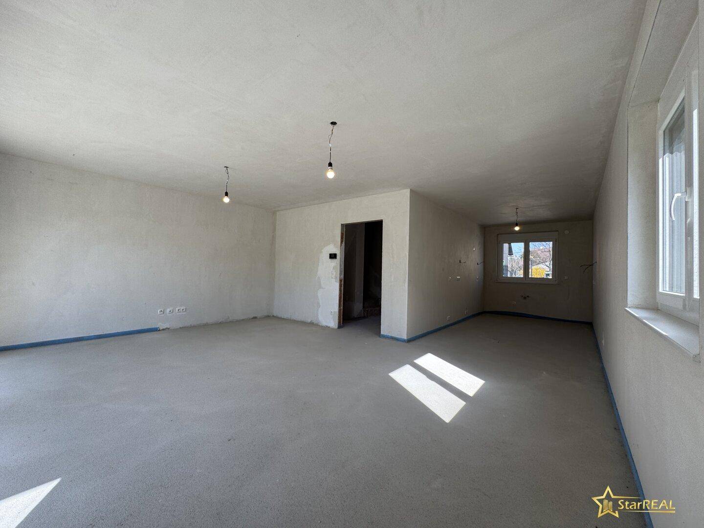 Heller, unfertiger Wohnbereich mit Fenster und Betonboden, der auf den Innenausbau wartet.