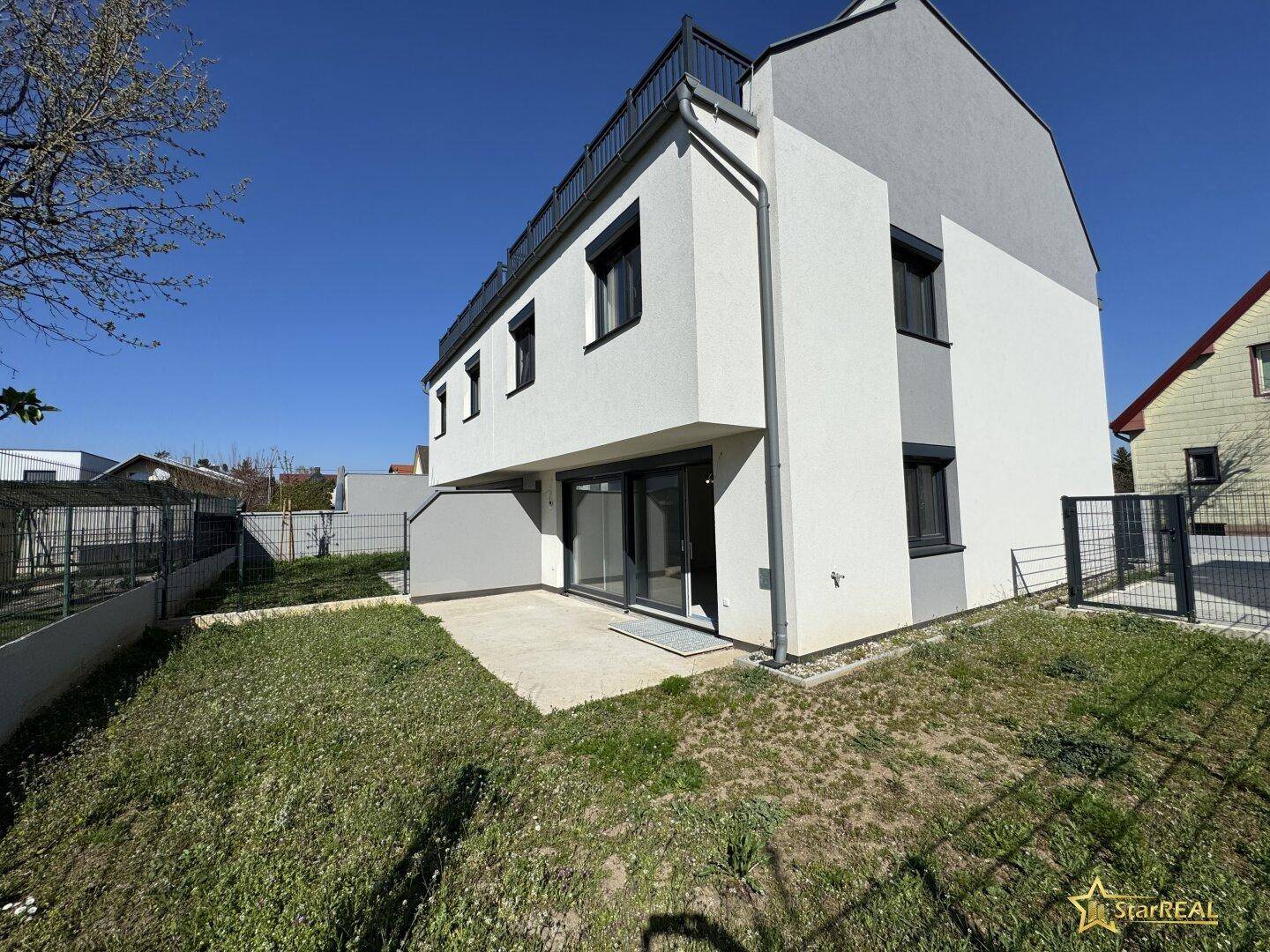 Außenansicht eines Neubaus mit kleiner Rasenfläche und Terrasse im Rohzustand.