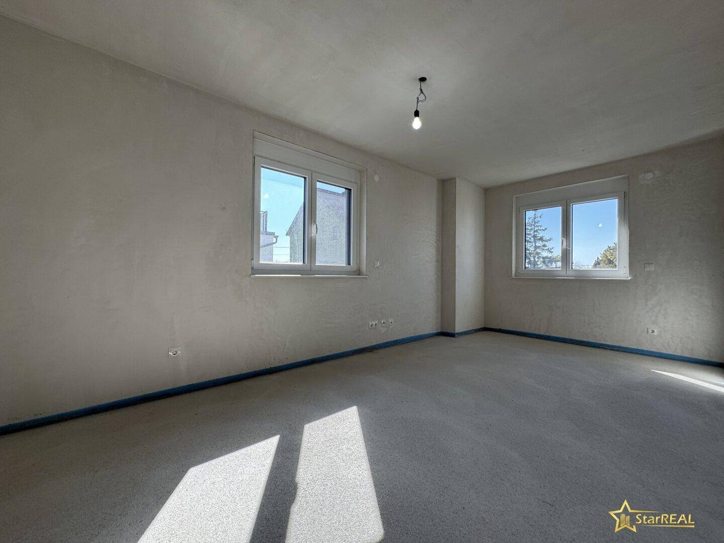 Heller, unfertiger Raum mit zwei Fenstern und Betonboden, ideal als Schlafzimmer.