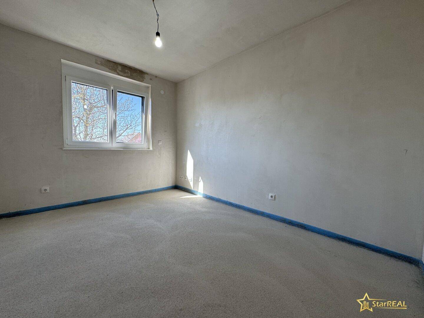 Unfertiges Schlafzimmer mit Fenster und Betonboden, bereit für den Innenausbau.