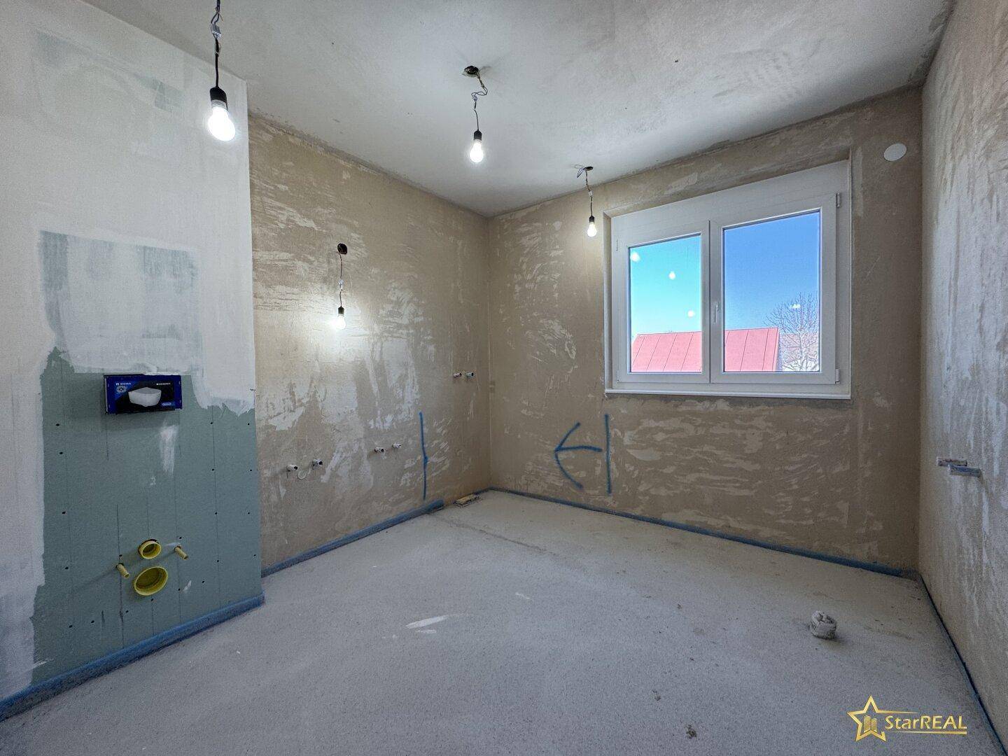 Unfertiges Badezimmer mit Rohinstallationen für Sanitäranlagen und Fenster.