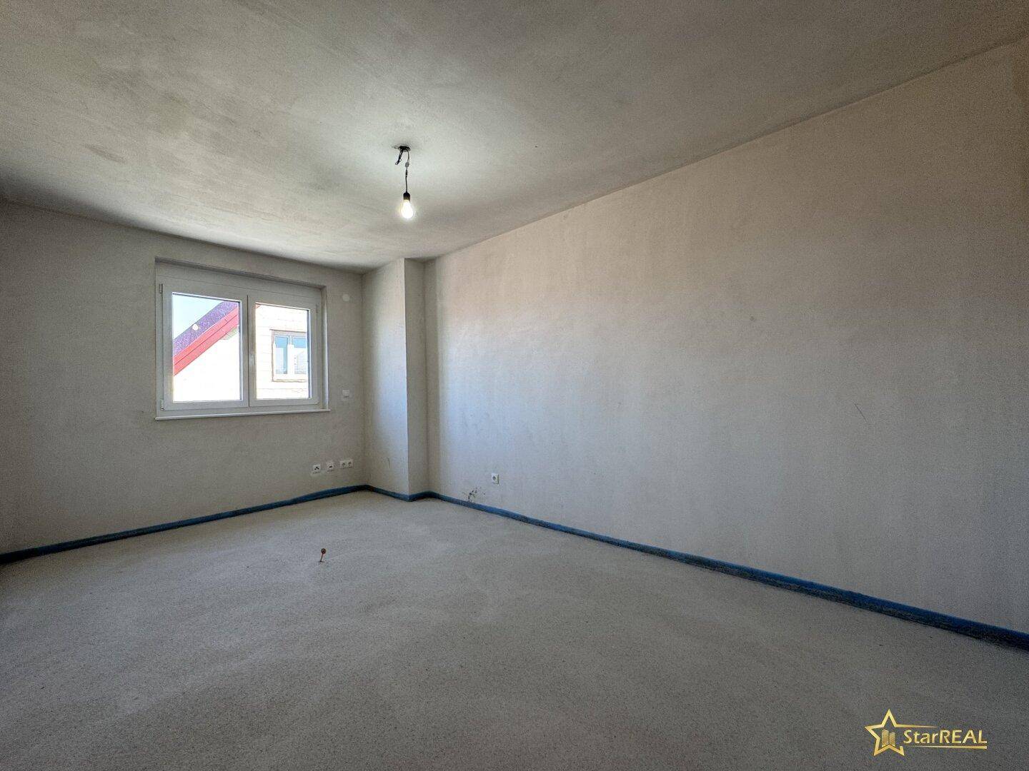Geräumiger, unfertiger Raum mit Fenster und Betonboden, ideal als Schlafzimmer.