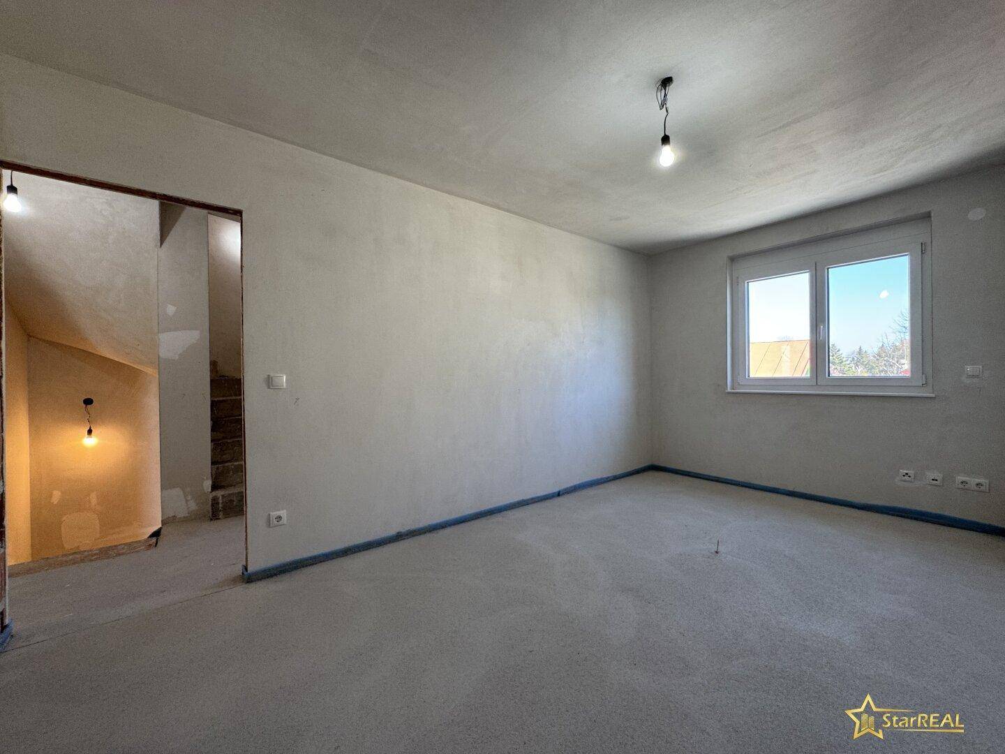 Unfertiges Schlafzimmer mit Fenster und Zugang zum Treppenhaus, bereit für den Ausbau.