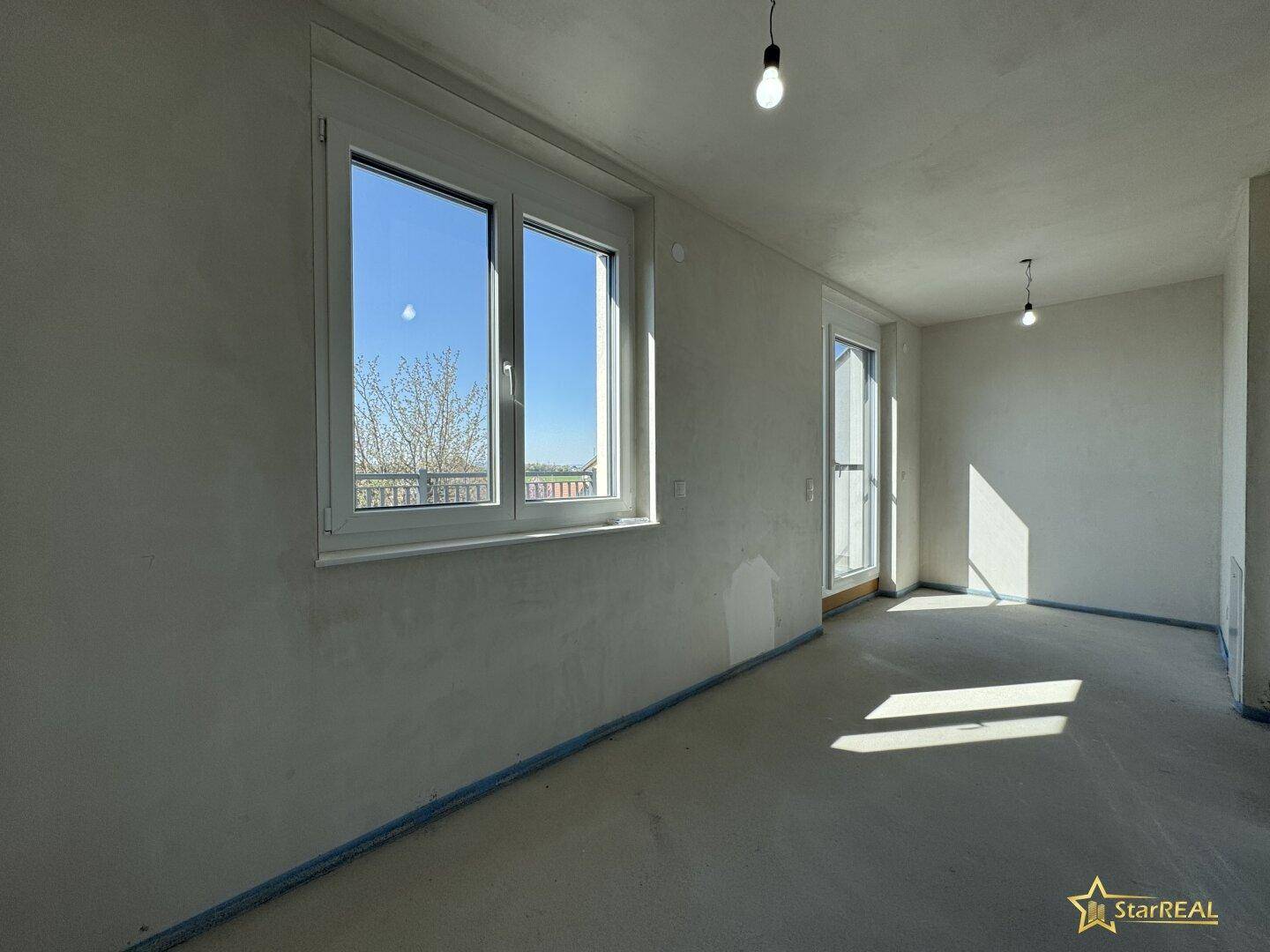 Heller, unfertiger Raum mit großem Fenster und Zugang zu einem Außenbereich.
